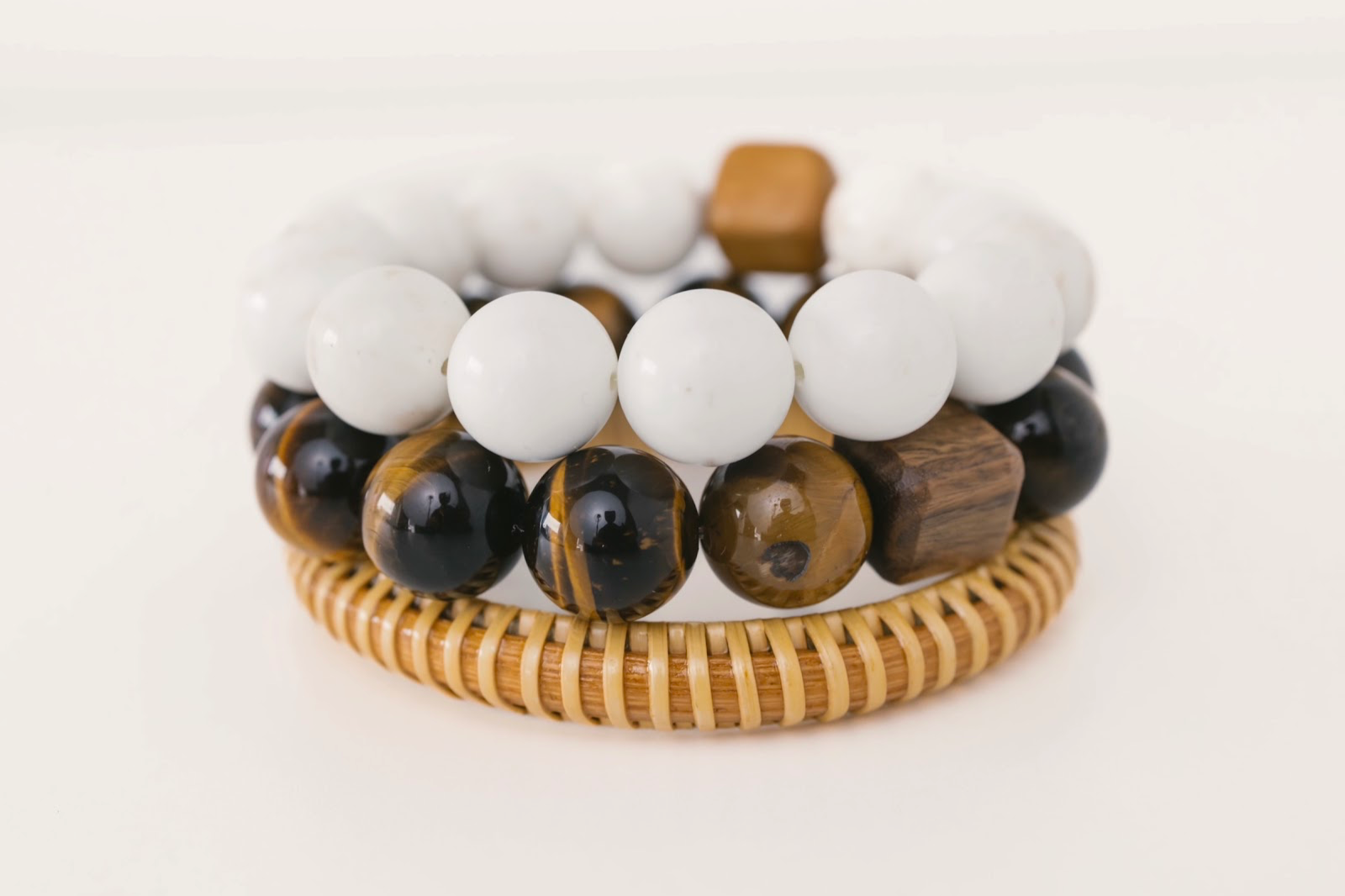 Two beaded bracelets displayed on a white background, one with white beads and the other with black and brown beads, both with a woven bracelet base.